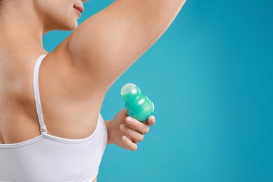 Photo of Young woman applying deodorant to armpit on teal background, closeup