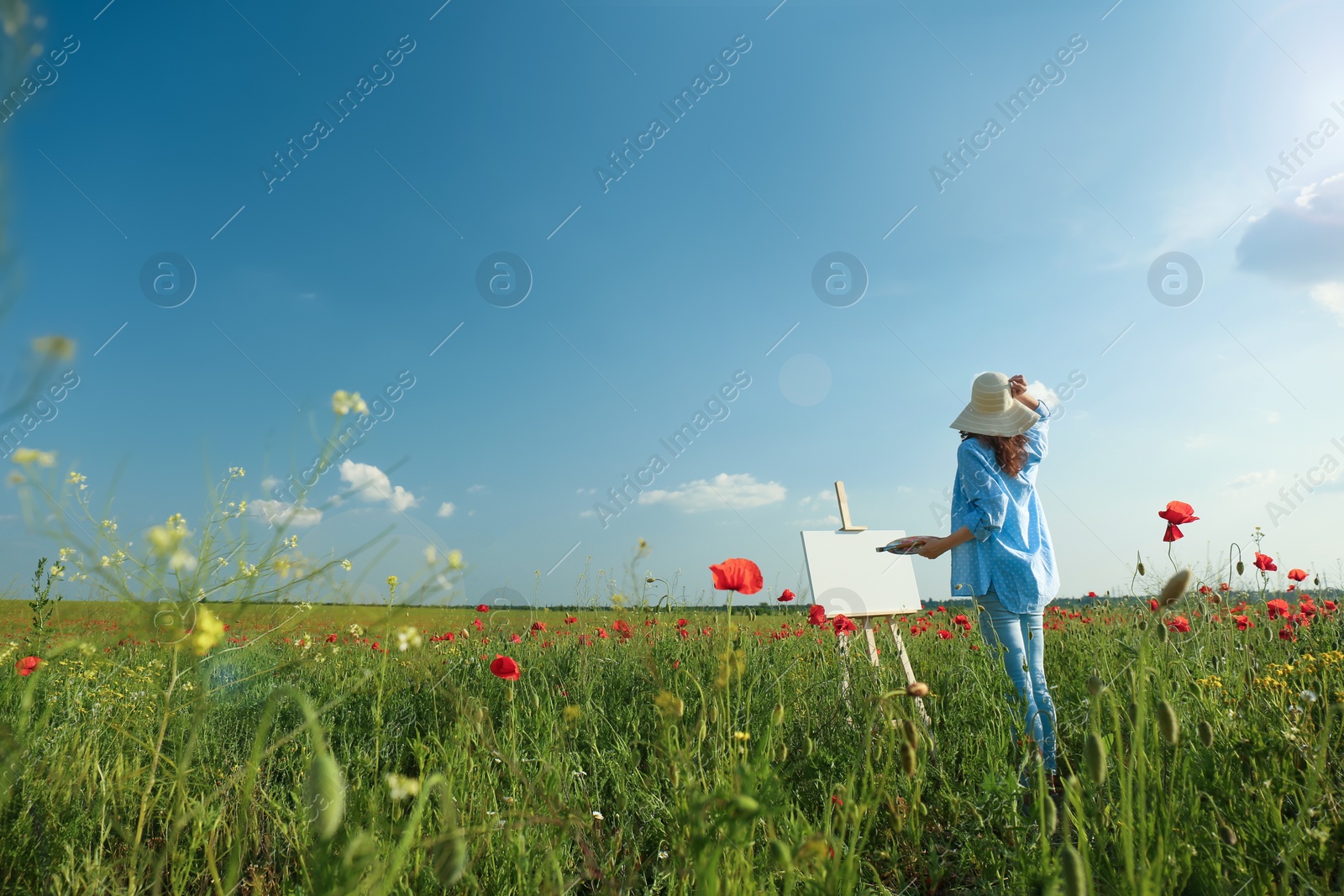 Photo of Woman painting on easel in beautiful poppy field