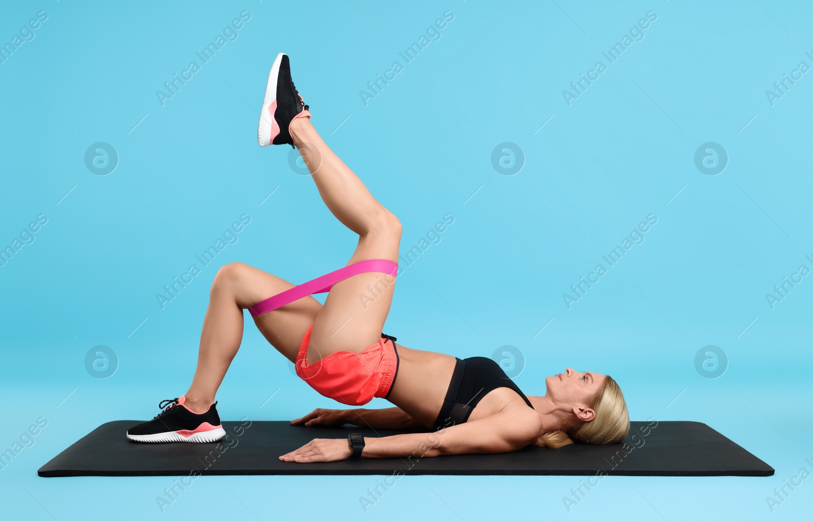 Photo of Woman exercising with elastic resistance band on fitness mat against light blue background