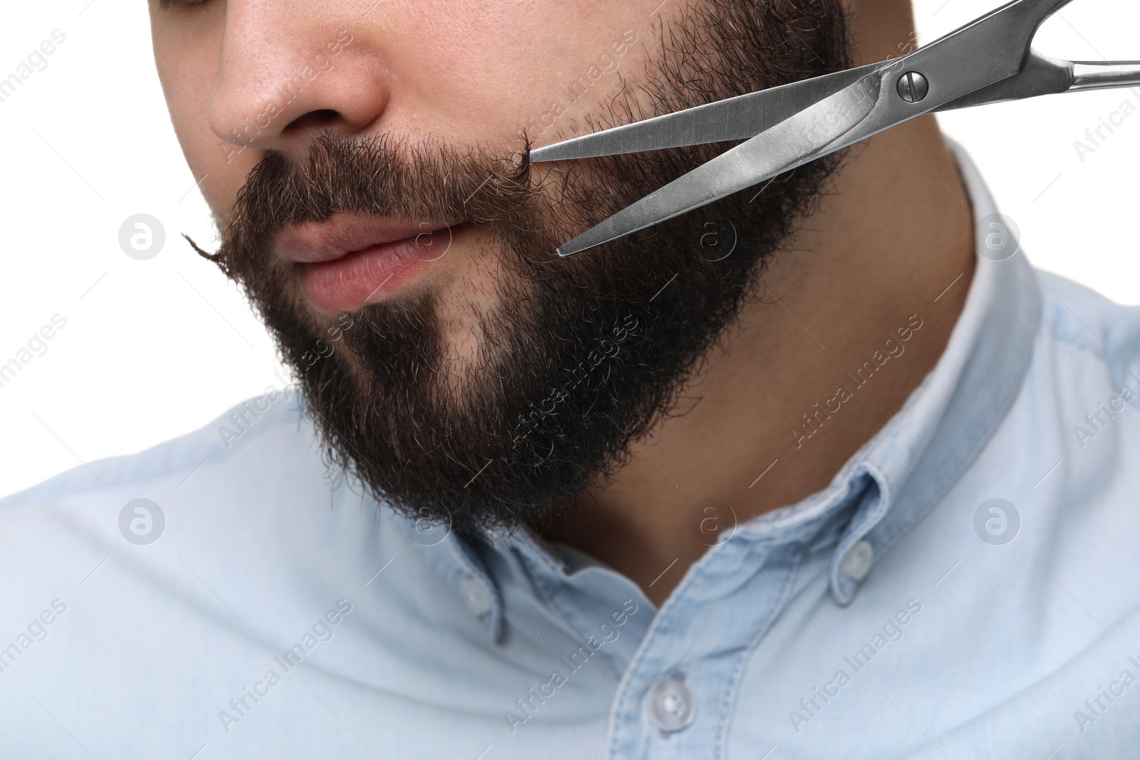 Photo of Handsome young man trimming beard with scissors on white background