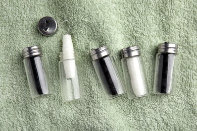 Photo of Biodegradable dental flosses in glass jars on light green towel, flat lay