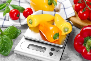 Photo of Kitchen scale with bell pepper among basil and tomatoes on grey textured table