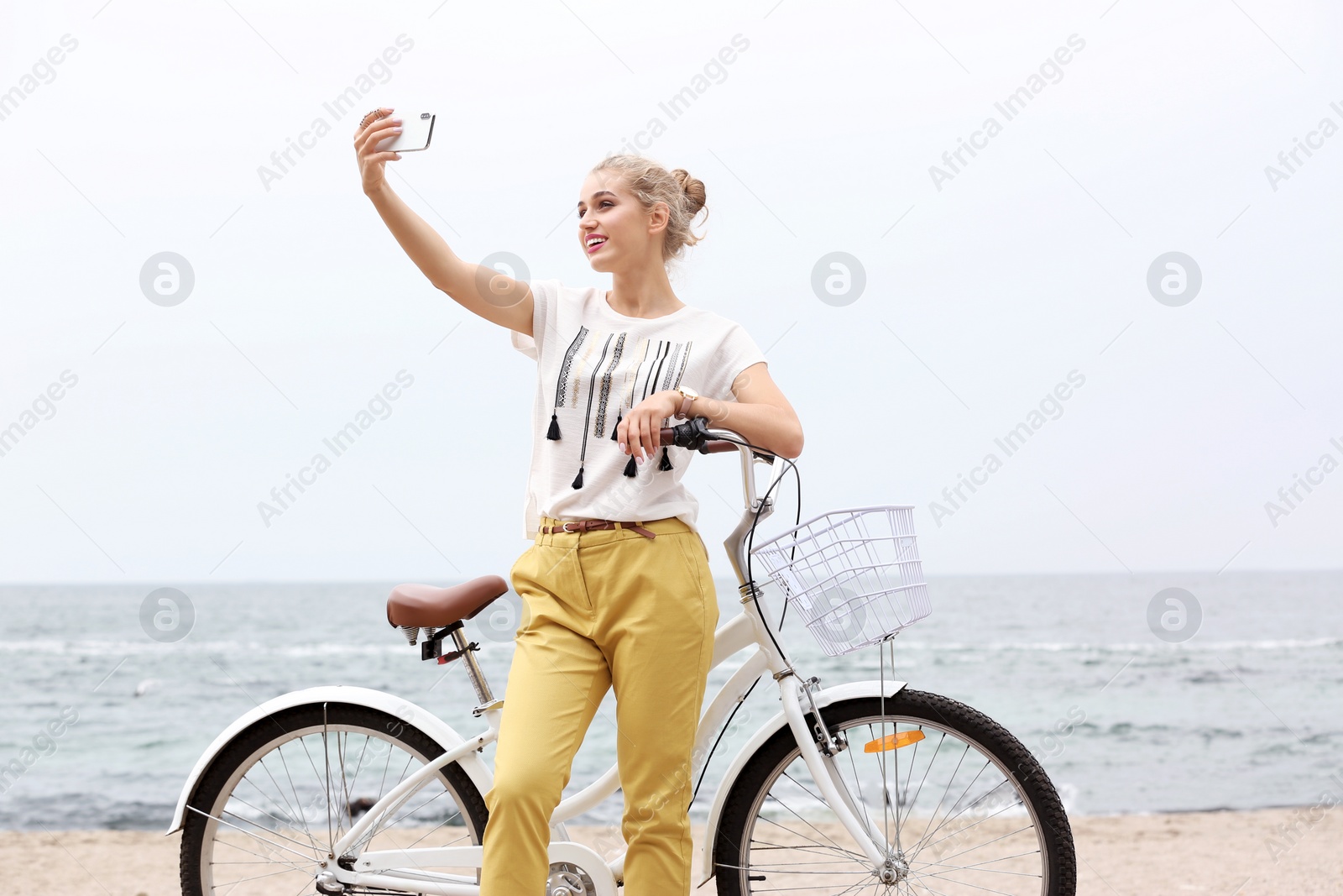 Photo of Attractive woman taking selfie near bicycle on sea coast