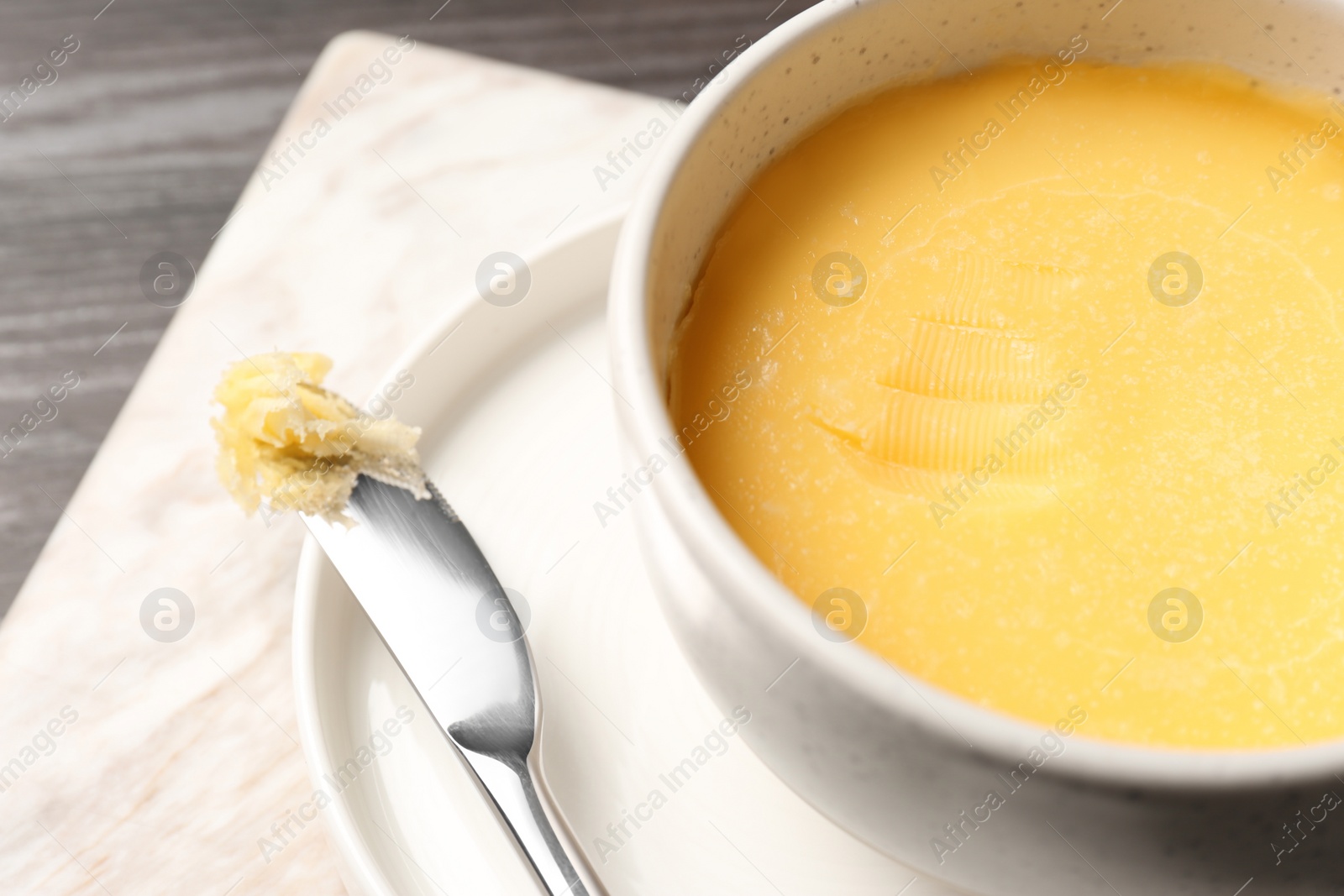 Photo of Bowl and knife with melting butter on table, closeup. Space for text