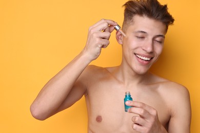 Photo of Handsome man applying serum onto his face on orange background