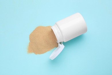 Medical bottle with beer yeast powder on light blue background, flat lay