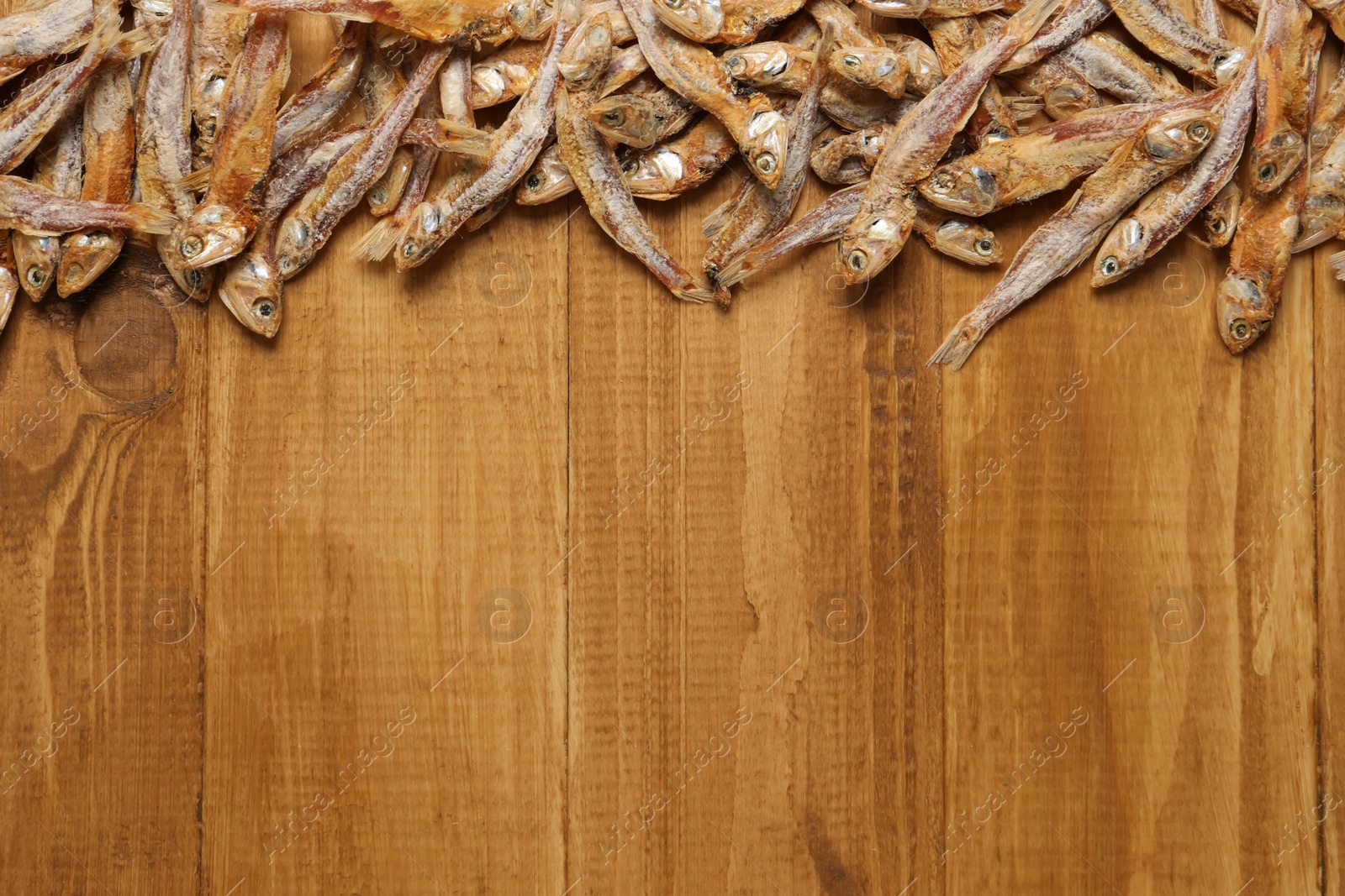 Photo of Tasty dried anchovies on wooden table, flat lay. Space for text