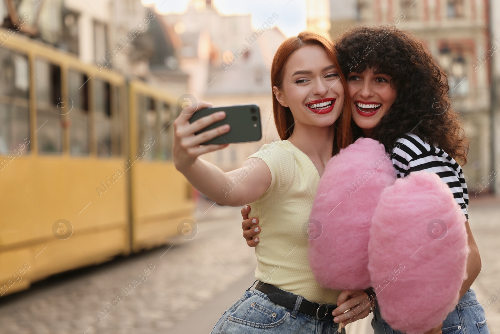 Photo of Happy friends with pink cotton candies taking selfie on city street. Space for text