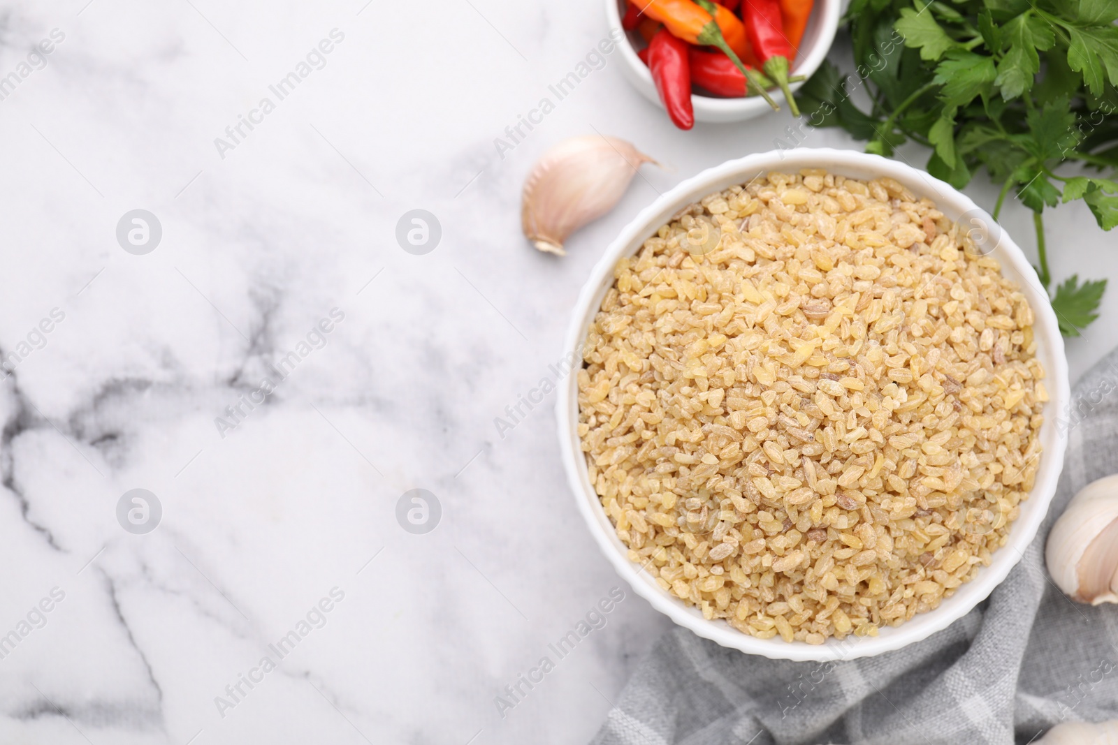 Photo of Raw bulgur in bowl and spices on marble table, flat lay. Space for text