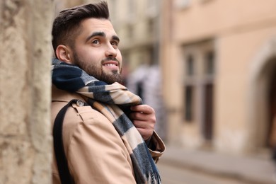 Photo of Smiling man in warm scarf on city street. Space for text