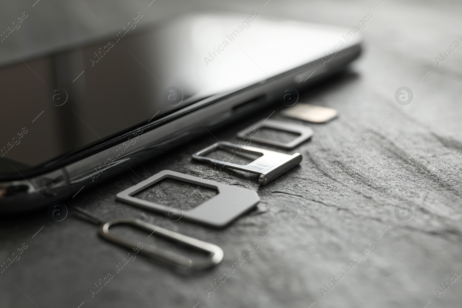 Photo of SIM card, mobile phone and ejector tool on grey table, closeup