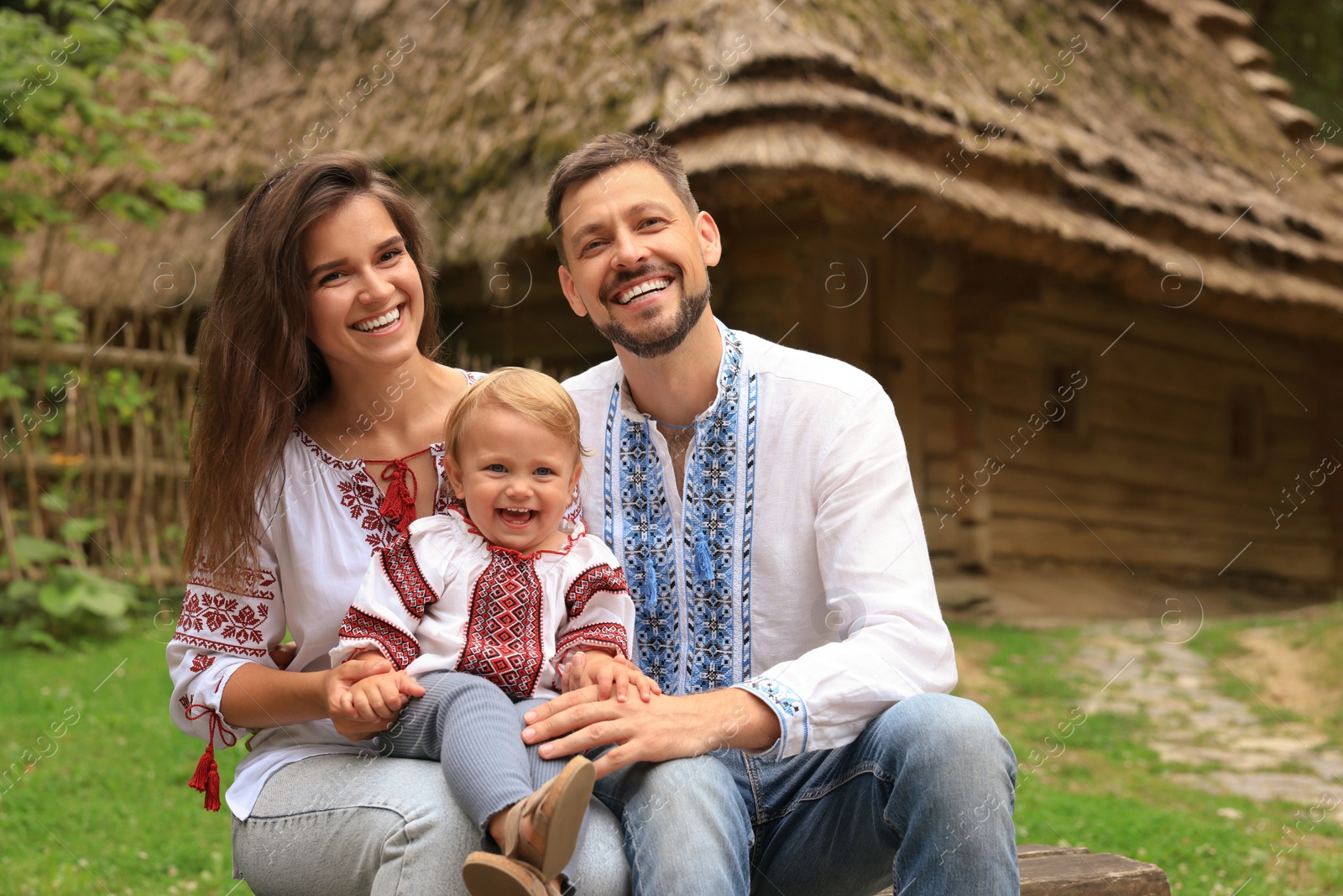 Photo of Happy family in Ukrainian national clothes sitting on bench outdoors