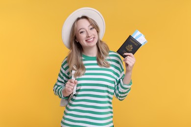 Happy young woman with passport, ticket and hat on yellow background