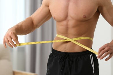 Photo of Athletic man measuring waist with tape at home, closeup. Weight loss concept