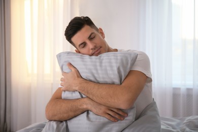 Photo of Man hugging pillow on bed with grey linens at home