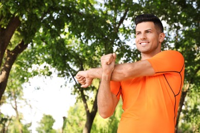 Photo of Handsome man in sportswear doing exercises outdoors on sunny day space for text