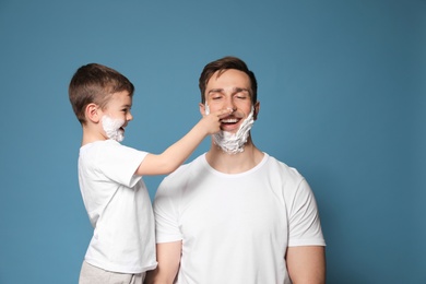 Photo of Dad and his little son having fun with shaving foam on faces against color background