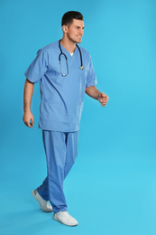 Handsome doctor in uniform walking on blue background