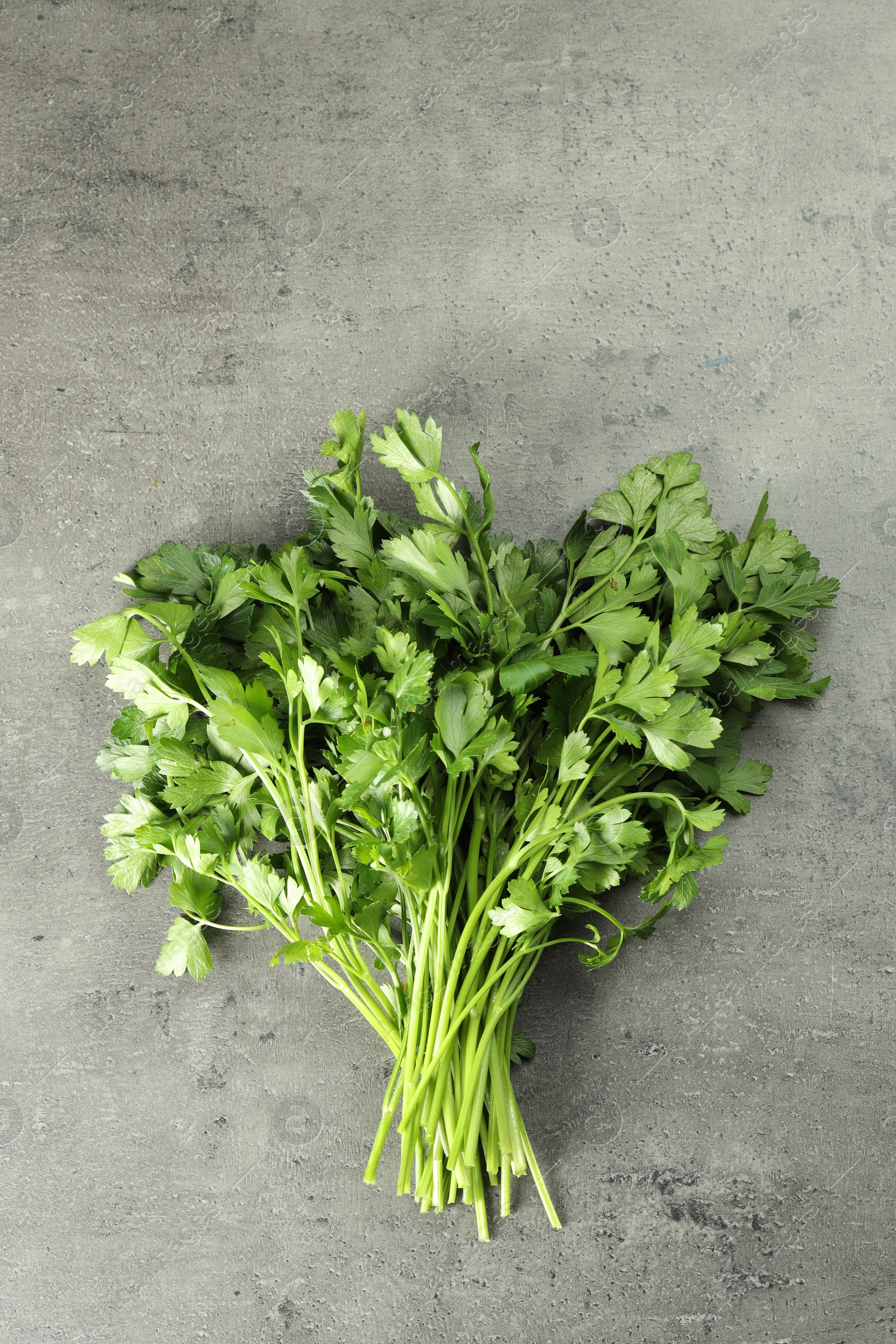 Photo of Bunch of fresh green parsley leaves on grey table, top view