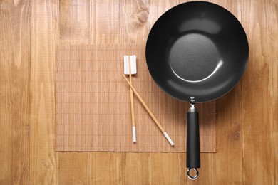 Empty iron wok and chopsticks on wooden table, top view. Space for text