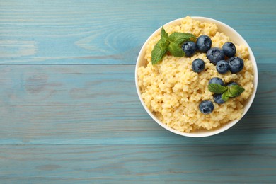 Photo of Tasty millet porridge with blueberries and mint in bowl on light blue wooden table, top view. Space for text