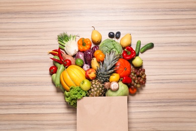 Paper bag with assortment of fresh organic fruits and vegetables on wooden table, flat lay