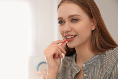 Young woman taking vitamin capsule on blurred background. Space for text