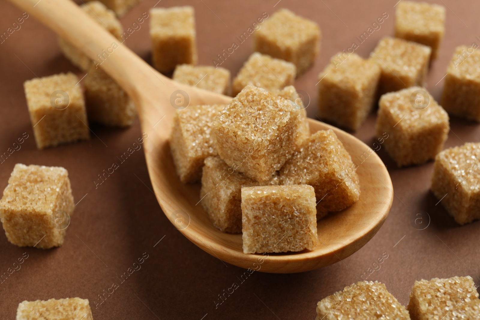 Photo of Brown sugar cubes and spoon on color background, closeup