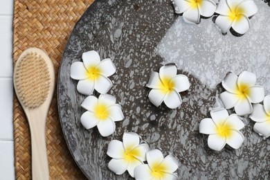 Photo of Bowl of water with plumeria flowers and brush on table, top view. Spa treatment