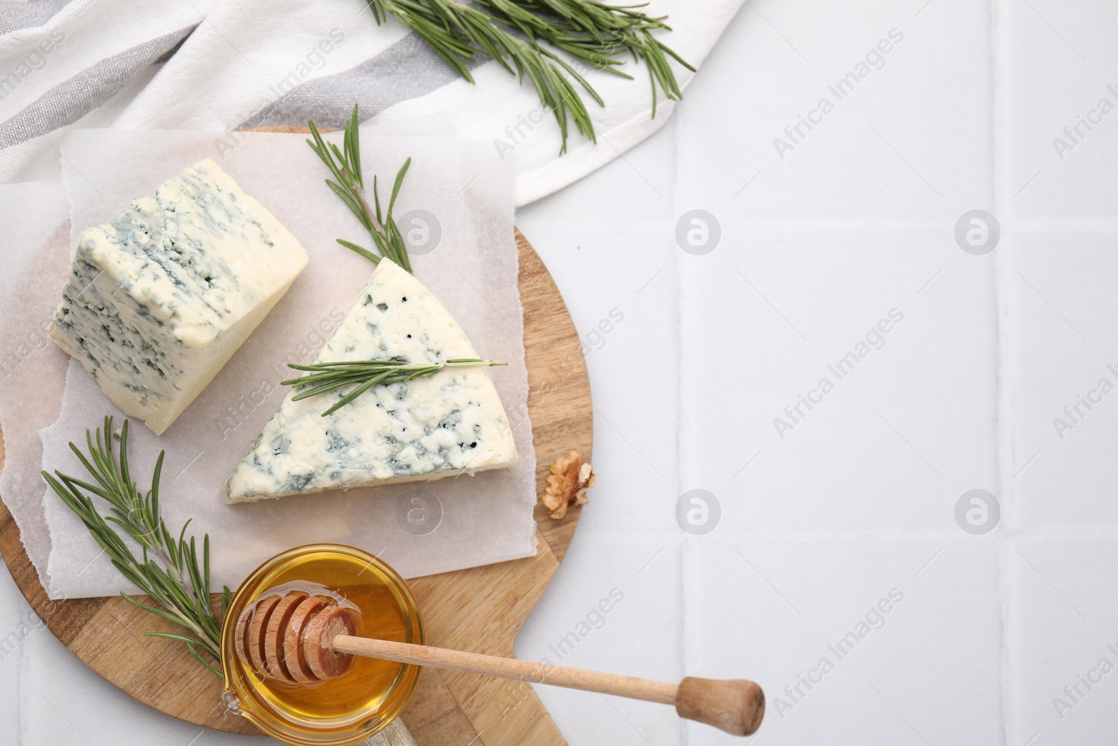 Photo of Tasty blue cheese with rosemary and honey on white tiled table, flat lay. Space for text
