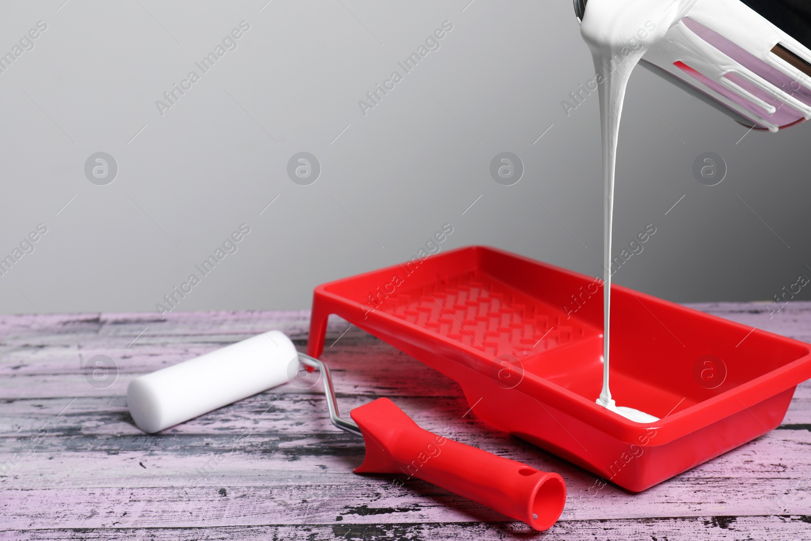 Photo of Pouring paint from can into tray on old pink wooden table