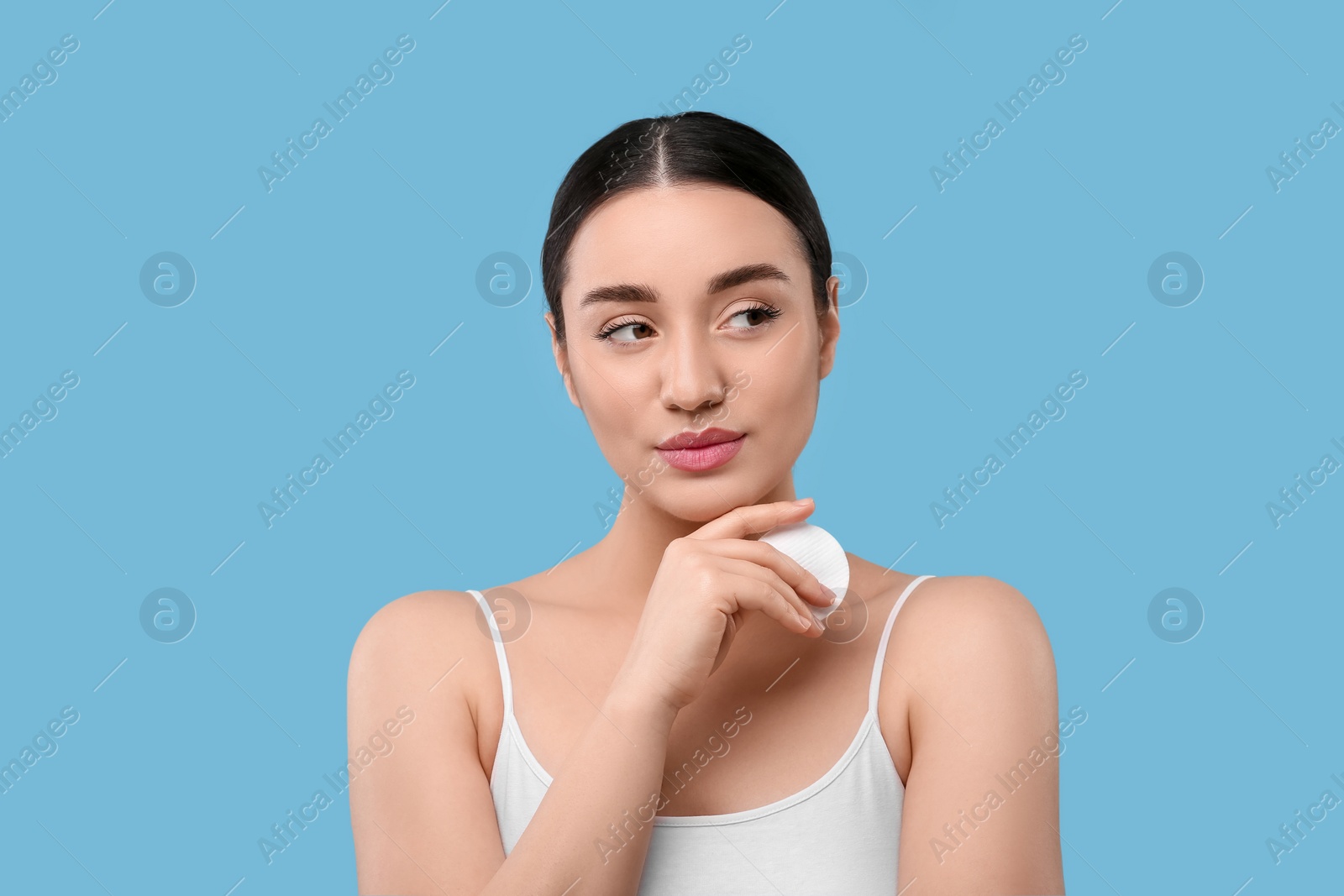 Photo of Beautiful woman with cotton pad on light blue background. Makeup removal