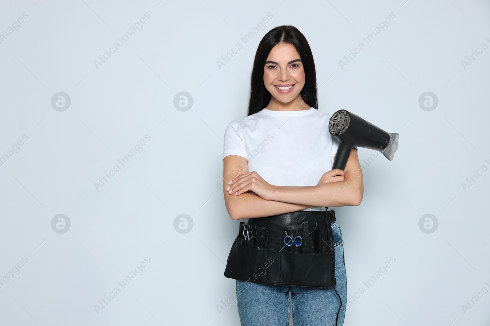 Photo of Portrait of happy hairdresser with hairdryer and professional tools on light background, space for text