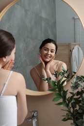 Photo of Young woman massaging her face near mirror in bathroom