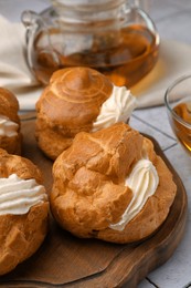 Photo of Delicious profiteroles filled with cream on white tiled table, closeup