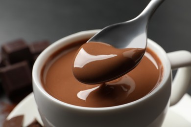 Photo of Spoon with yummy hot chocolate over cup, closeup