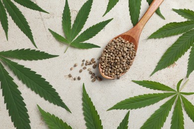 Photo of Fresh green hemp leaves and spoon with seeds on light grey table, flat lay