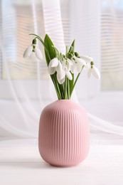 Photo of Beautiful snowdrops in vase on white wooden table indoors