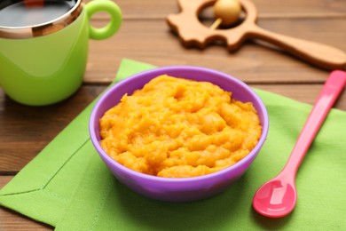 Plastic dishware with healthy baby food on wooden table, closeup