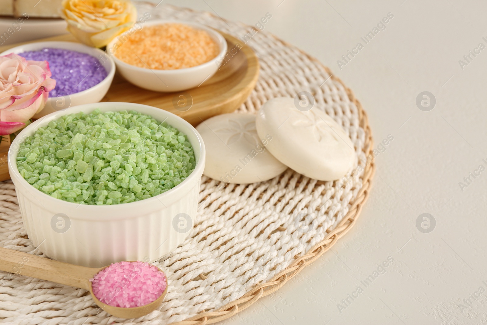 Photo of Bowls with different sea salt, soap bars and rose on light grey table. Space for text