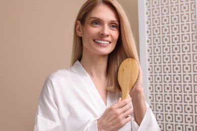 Photo of Beautiful woman in white robe brushing her hair indoors