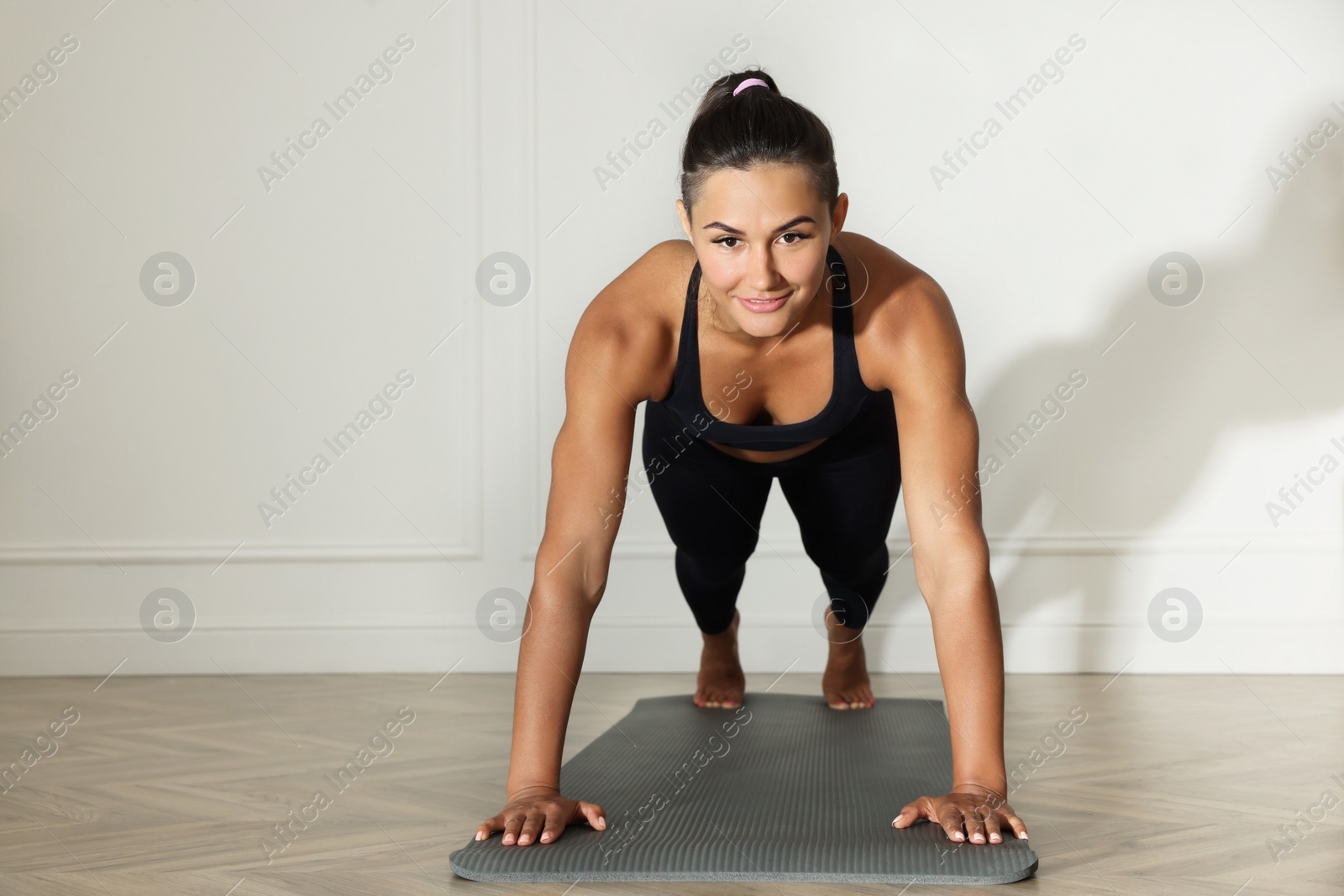 Photo of Young woman doing plank exercise near white wall