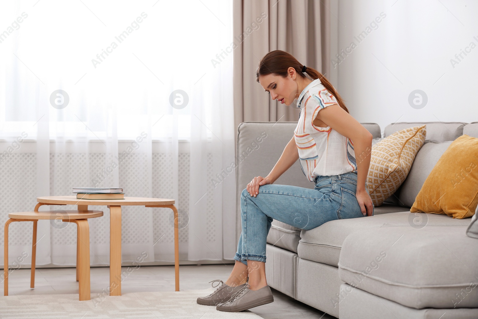 Photo of Young woman suffering from hemorrhoid on sofa at home