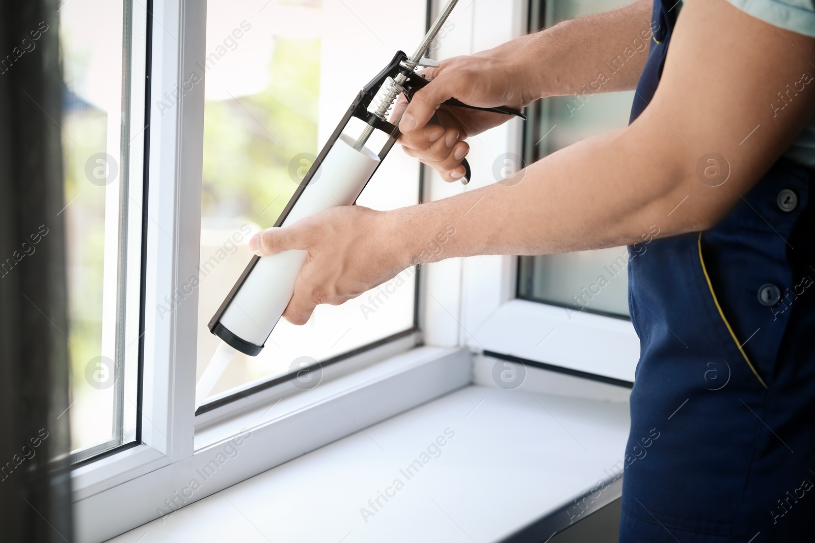 Photo of Construction worker sealing window with caulk indoors