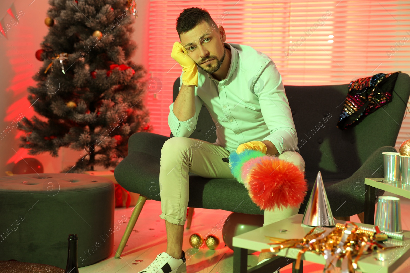 Photo of Man with dusting brush suffering from hangover in messy room after New Year party