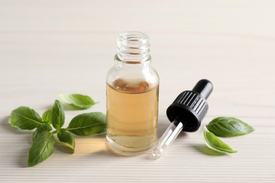 Photo of Glass bottle of basil essential oil and leaves on white  wooden table