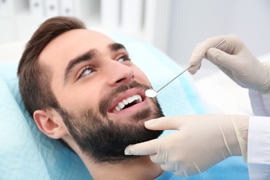 Photo of Dentist examining young man's teeth with mirror in hospital