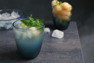 Glass with tasty melon ball drink on table against dark background. Space for text