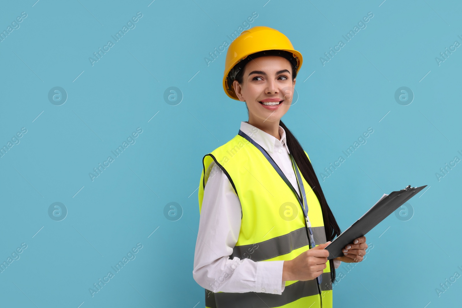 Photo of Engineer in hard hat holding clipboard on light blue background, space for text