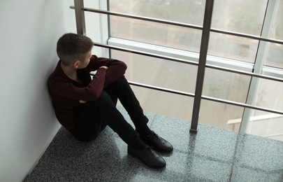 Upset boy sitting near window indoors. Space for text